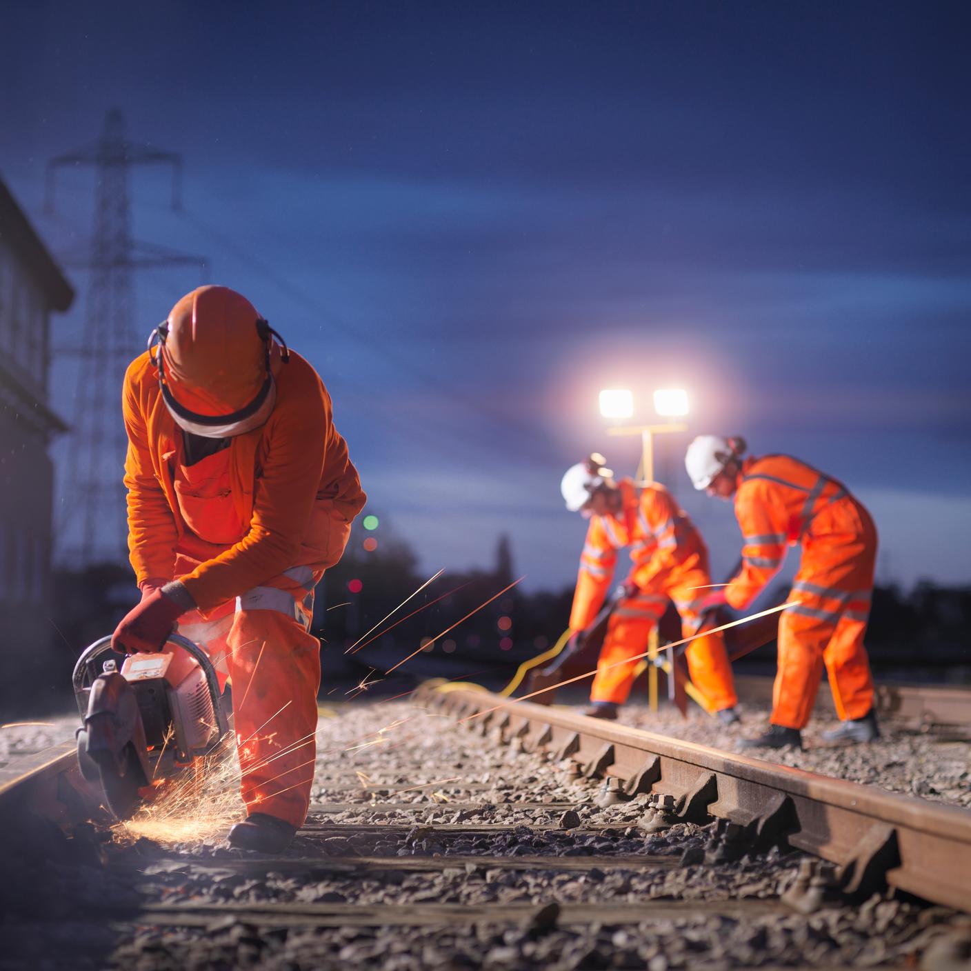 Railway maintenance workers using grinder on track at night