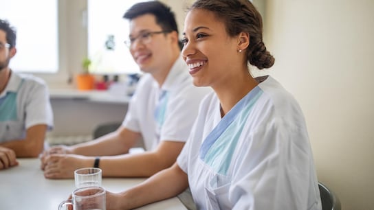 African female nurse sitting with coworkers in hospital during break.