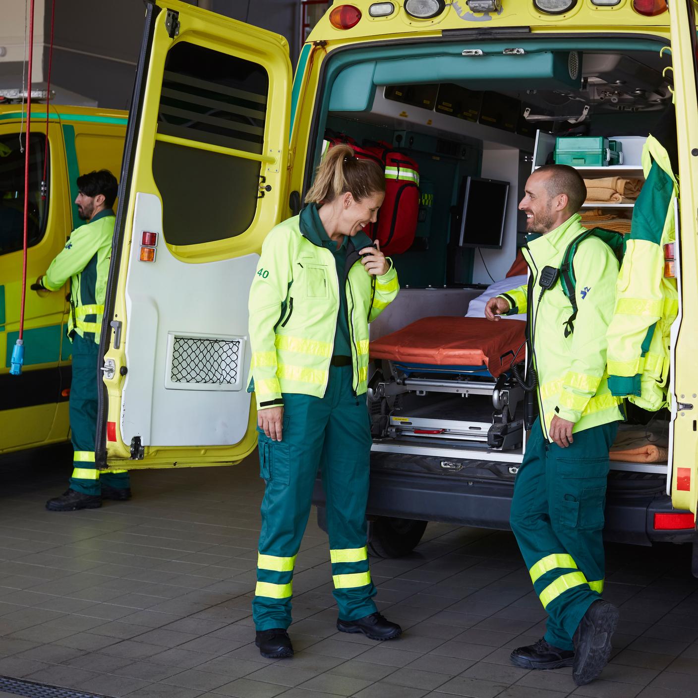 Paramedic looking at coworker talking on walkie-talkie while standing by ambulance in parking lot