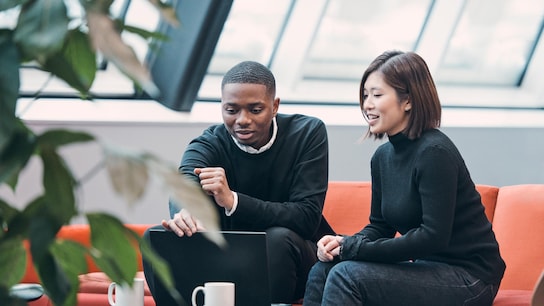 Colleagues talking over coffee while looking at a laptop